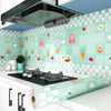 A kitchen splashback wall decorated with light green tiles featuring colorful food illustrations and a roll of self-adhesive 