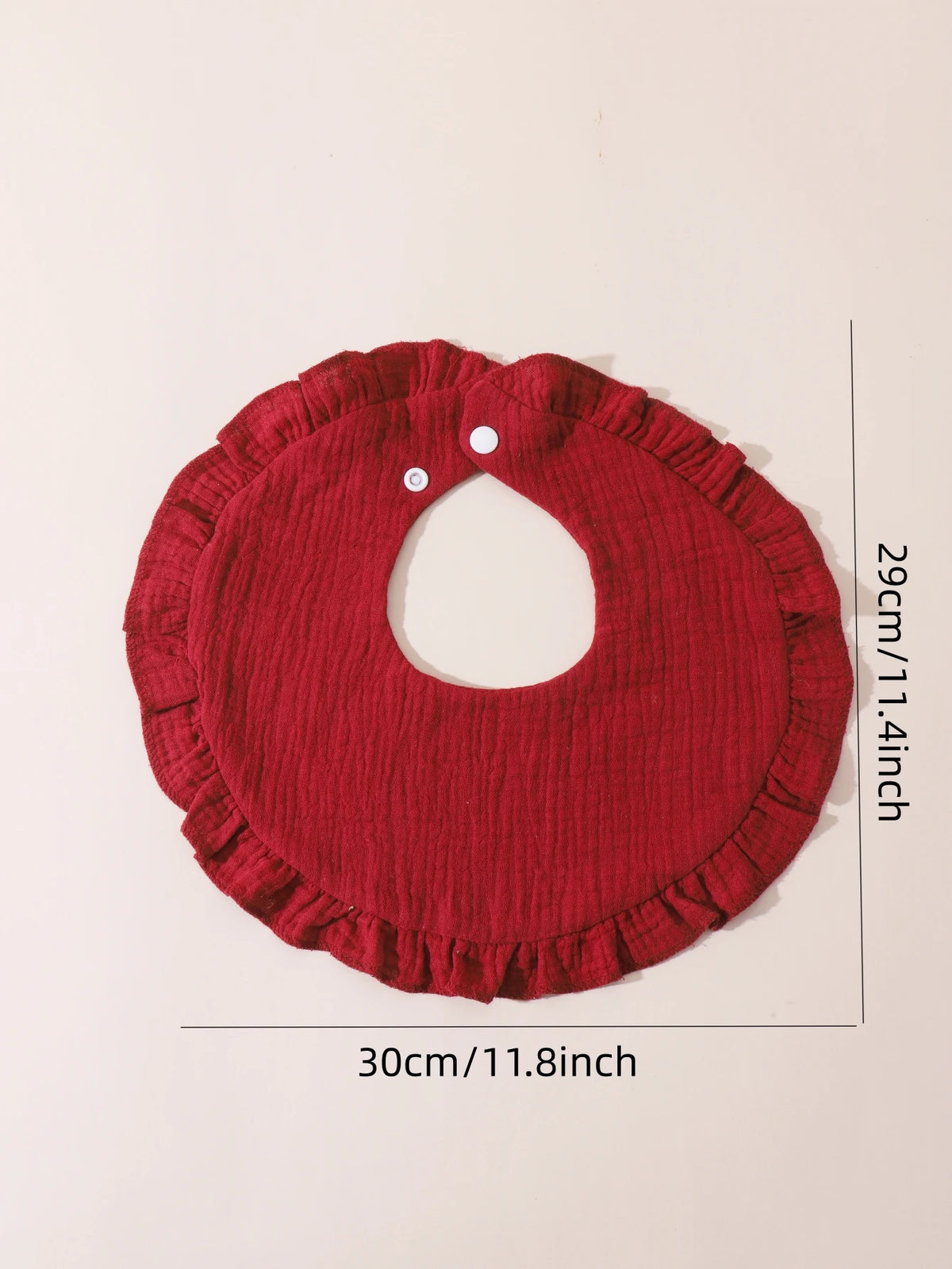 A red knitted baby bib with a ruffled trim shown flat, measuring 29cm wide.
