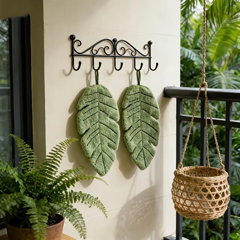 Two green banana leaves are displayed on a wall hook, suggesting an absorbent hand towel product.