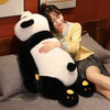 A woman is posing with a large black and white panda plush toy on a gray sofa.