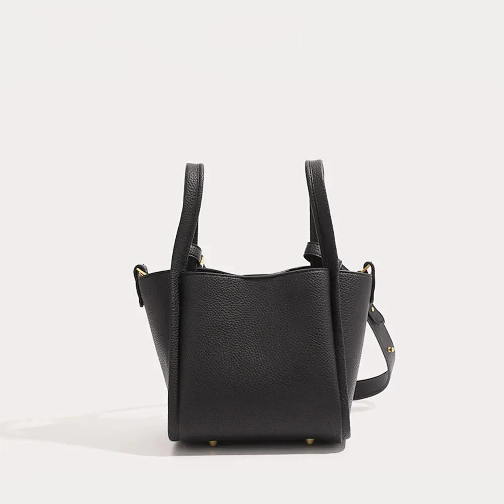 A black minimalist vegan leather crossbody bucket bag with gold hardware shown against a light background.