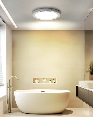 Modern white oval bathtub in a bright bathroom with recessed lighting and a window.