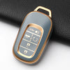 A close-up view of a metallic gold Honda key fob cover with buttons and a protective case resting on a black fabric.