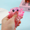 A hand holds a pink, glittery axolotl squishy stress ball with an air vent against a light blue background.