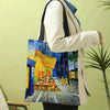 A person holds a canvas tote bag featuring a Van Gogh style painting of a street scene.