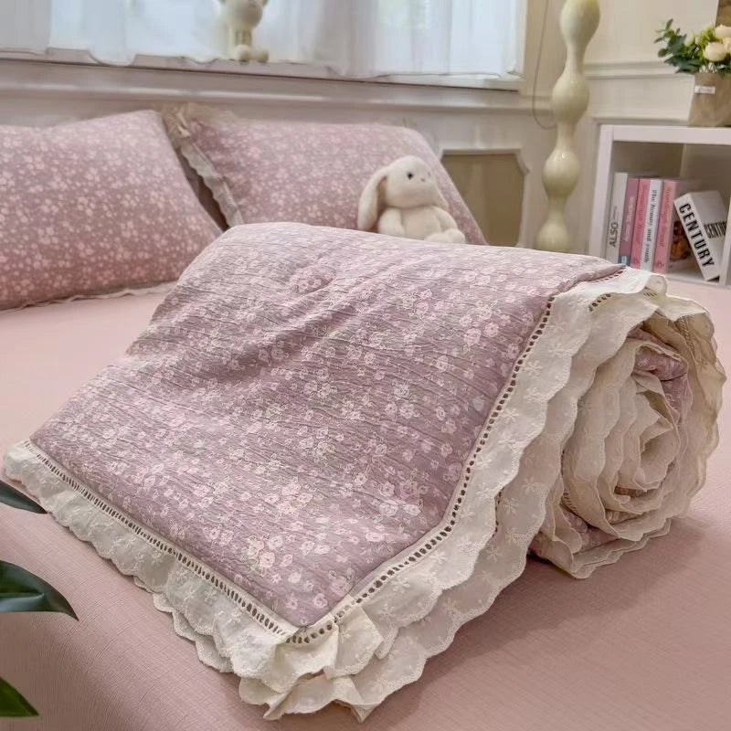 A rolled floral washed cotton gauze summer quilt in mauve pink with white lace trim.