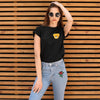 A woman models a black t-shirt with a yellow embroidered patch and blue jeans against a wooden background.