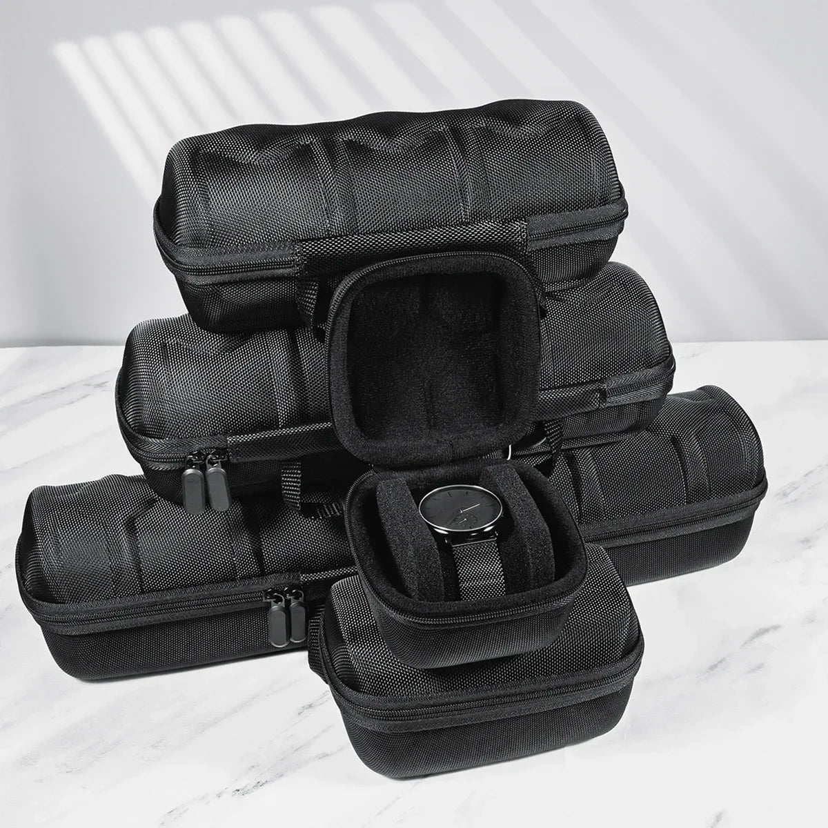 A stack of black portable leather watch travel cases with soft lining resting on a white marble surface.