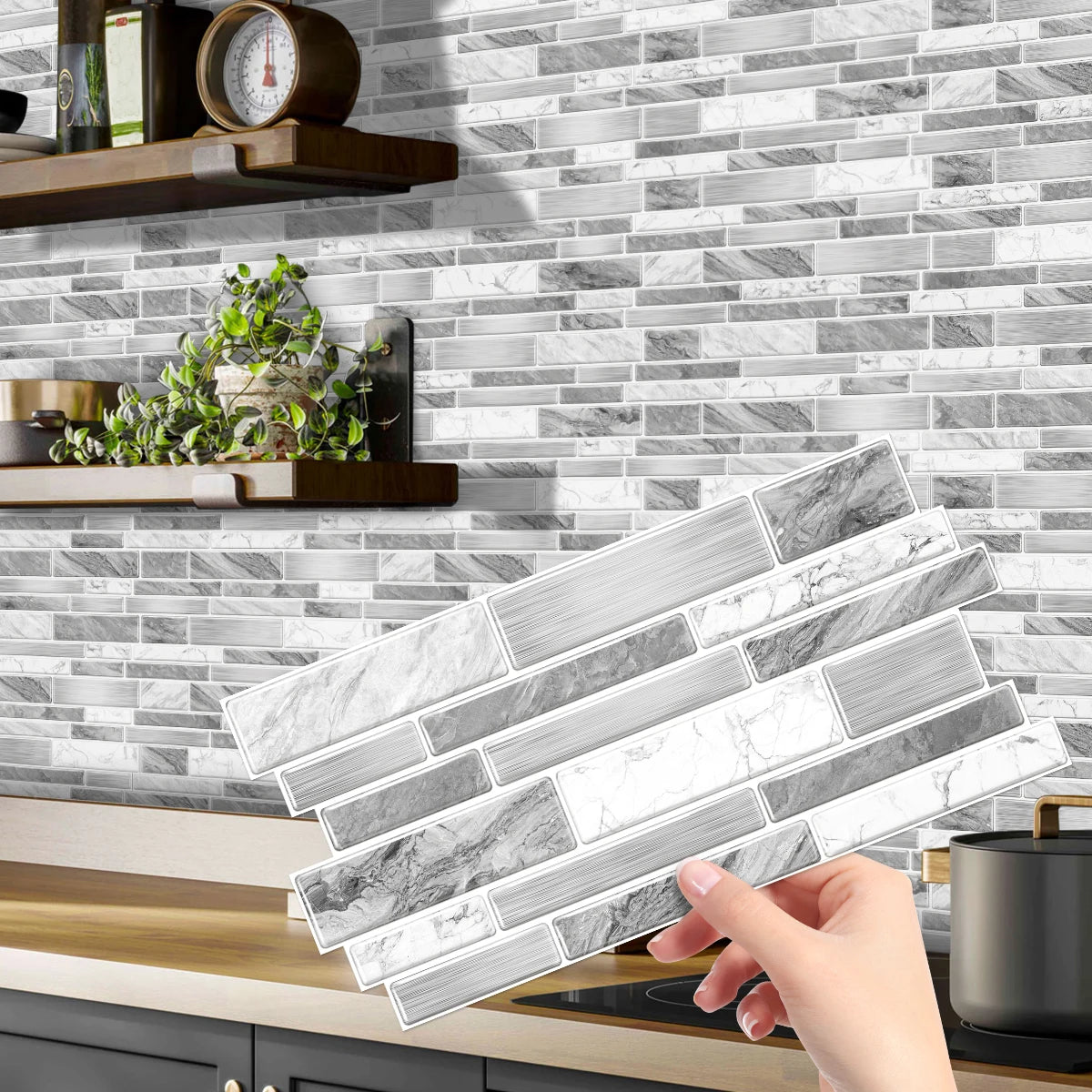 A hand holds a rectangular peel-and-stick tile sticker for kitchen backsplash against a gray and white marble subway tile bac