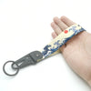A hand holds a keychain featuring a blue and white Kanagawa surf design on a light yellow strap.