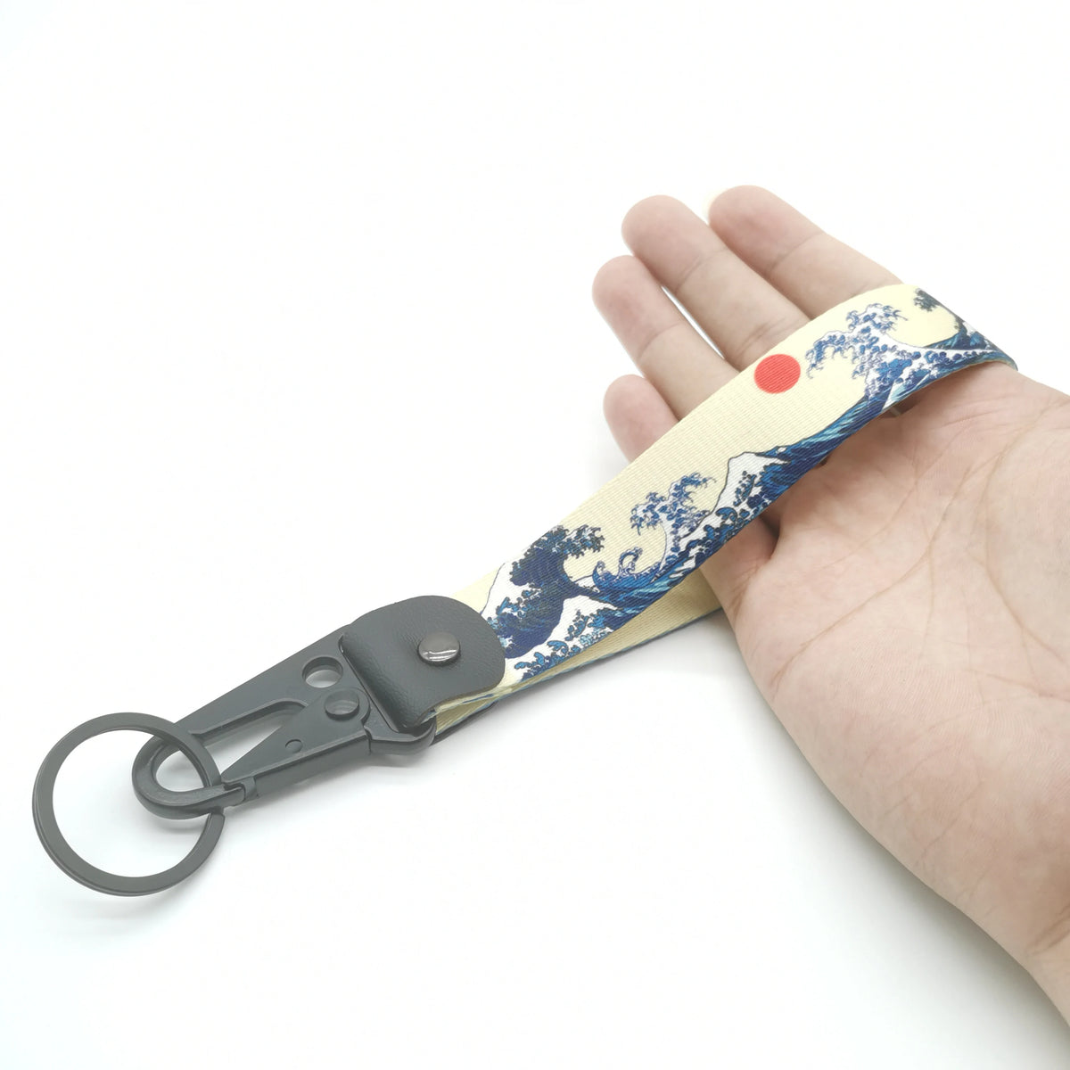 A hand holds a keychain featuring a blue and white Kanagawa surf design on a light yellow strap.