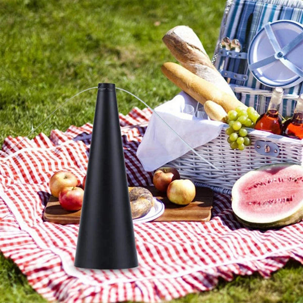 A black portable fly repellent fan is displayed on a red and white checkered cloth with fruit and a woven basket in the backg