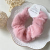 A pink plush coil hair tie is displayed on a white plate with a silver rim and a tag.