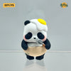 A cute blind box panda figure with white fur, black patches, and a yellow highlight on its head, holding a small gray spoon.