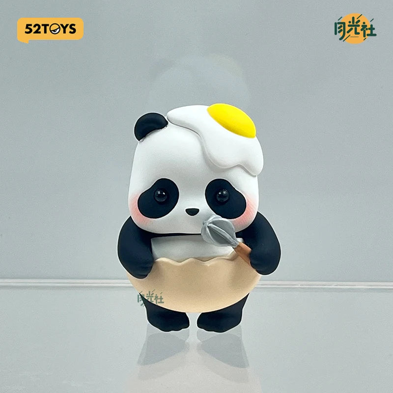 A cute blind box panda figure with white fur, black patches, and a yellow highlight on its head, holding a small gray spoon.