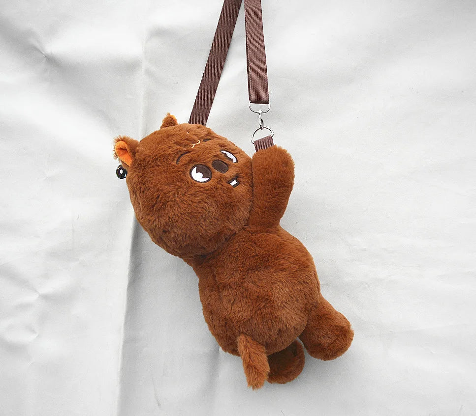 A brown, fluffy teddy bear plush doll hanging by a strap against a white background.