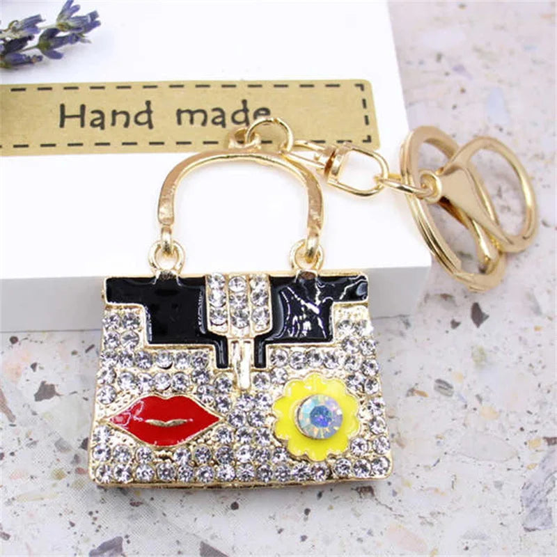 A gold-toned handbag keychain featuring black and white patterns with red lips and a yellow flower detail.