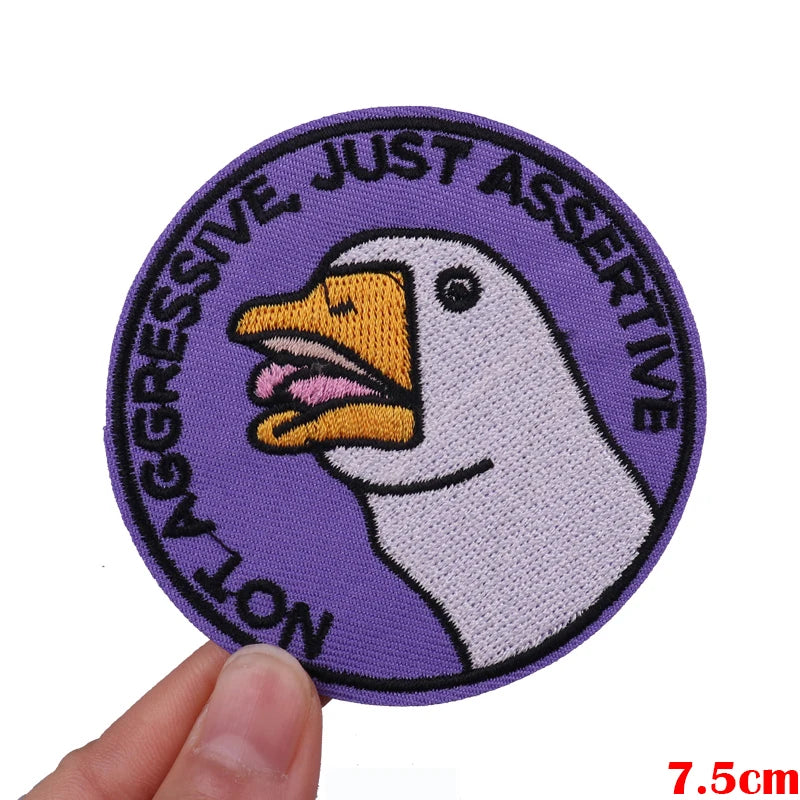 Purple embroidered patch featuring a white duck face with text reading Not Aggressive Just Assertive