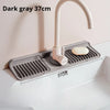 Dark gray silicone faucet splash mat with a curved metal faucet and soap dish placed in a white sink.