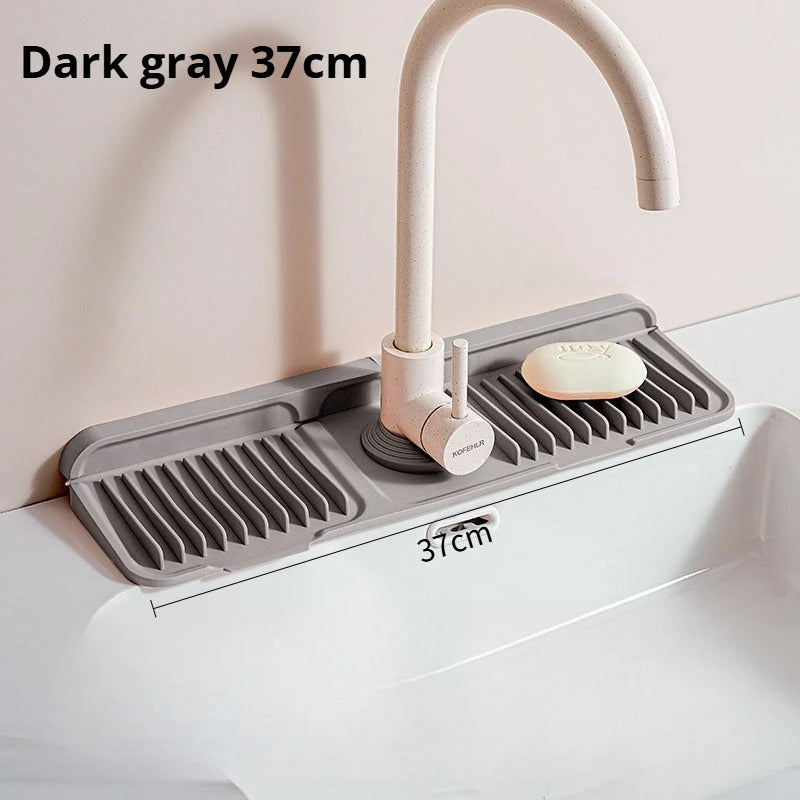 Dark gray silicone faucet splash mat with a curved metal faucet and soap dish placed in a white sink.