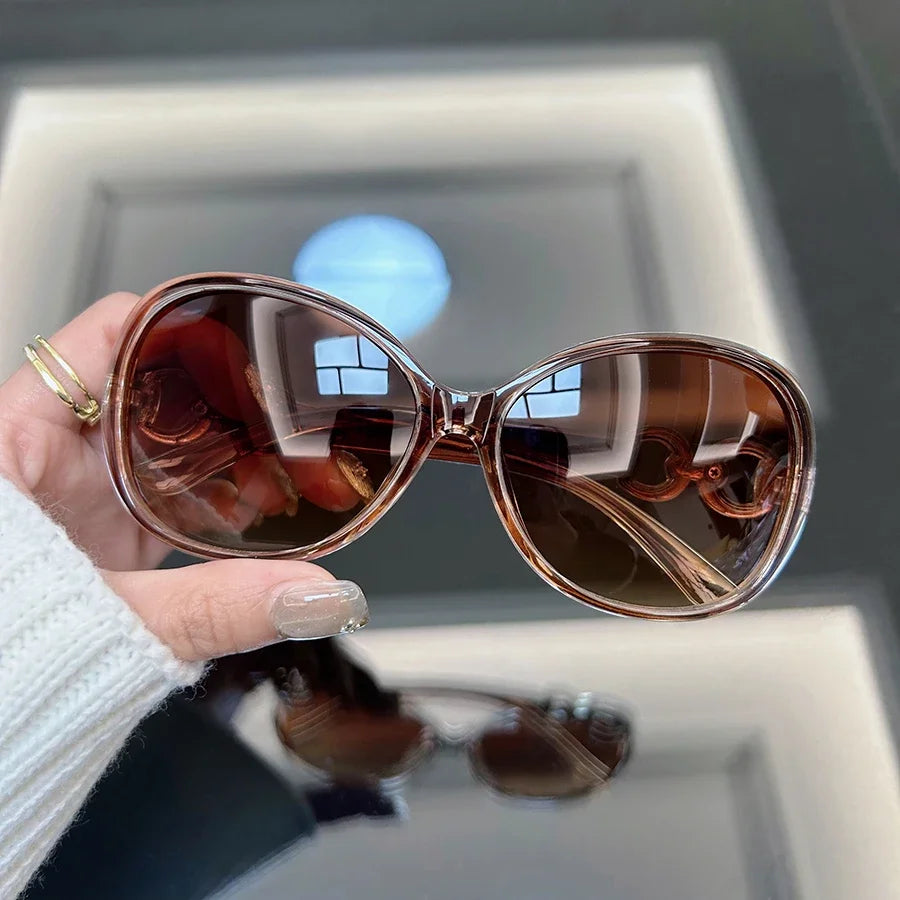 A hand holds a pair of brown tinted square vintage sunglasses against a light background.
