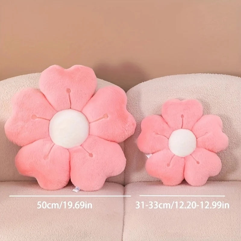 A pink plush daisy flower throw pillow with a white center resting on a light colored sofa.