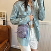 A person wearing a light blue denim shirt and white top holds a lavender crossbody bag with a pink strap.