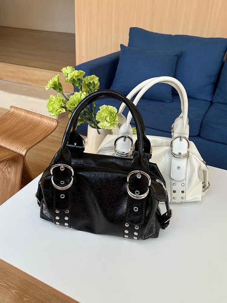 A black soft PU leather shoulder bag with silver rivet accents resting on a white table.