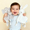 A baby is holding a gray elephant plush toy with a comfort blanket and a white rabbit plush toy.