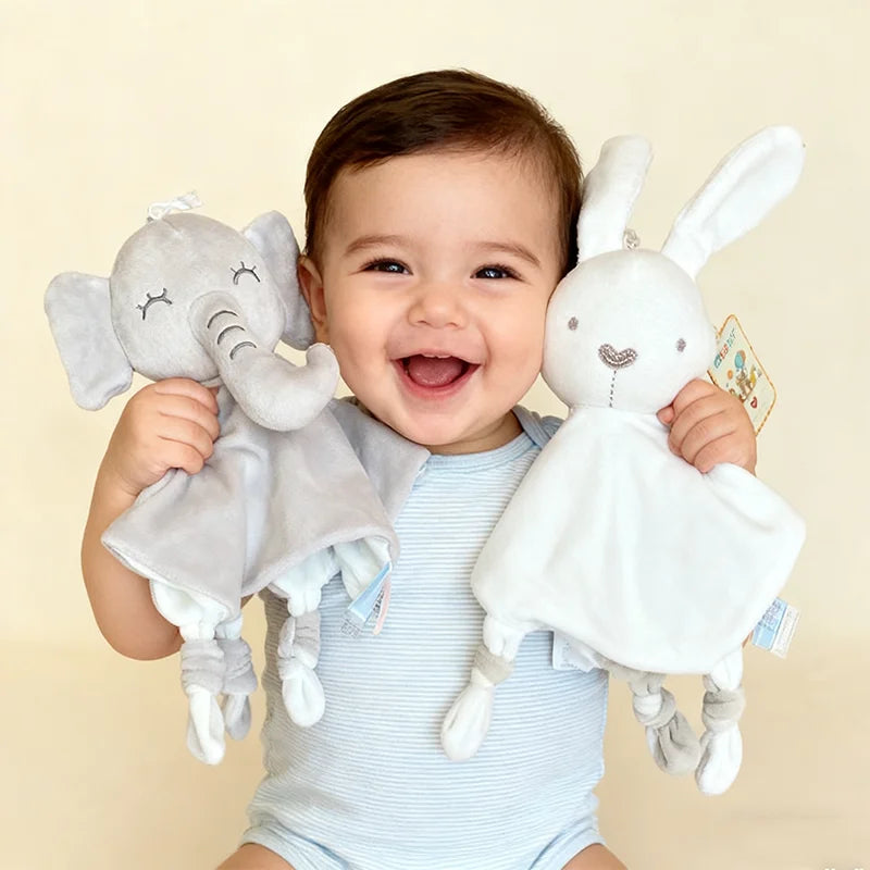 A baby is holding a gray elephant plush toy with a comfort blanket and a white rabbit plush toy.