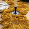 A golden yellow crinkle gauze cheesecloth table runner draped on a wooden surface with silverware and a white candle holder.