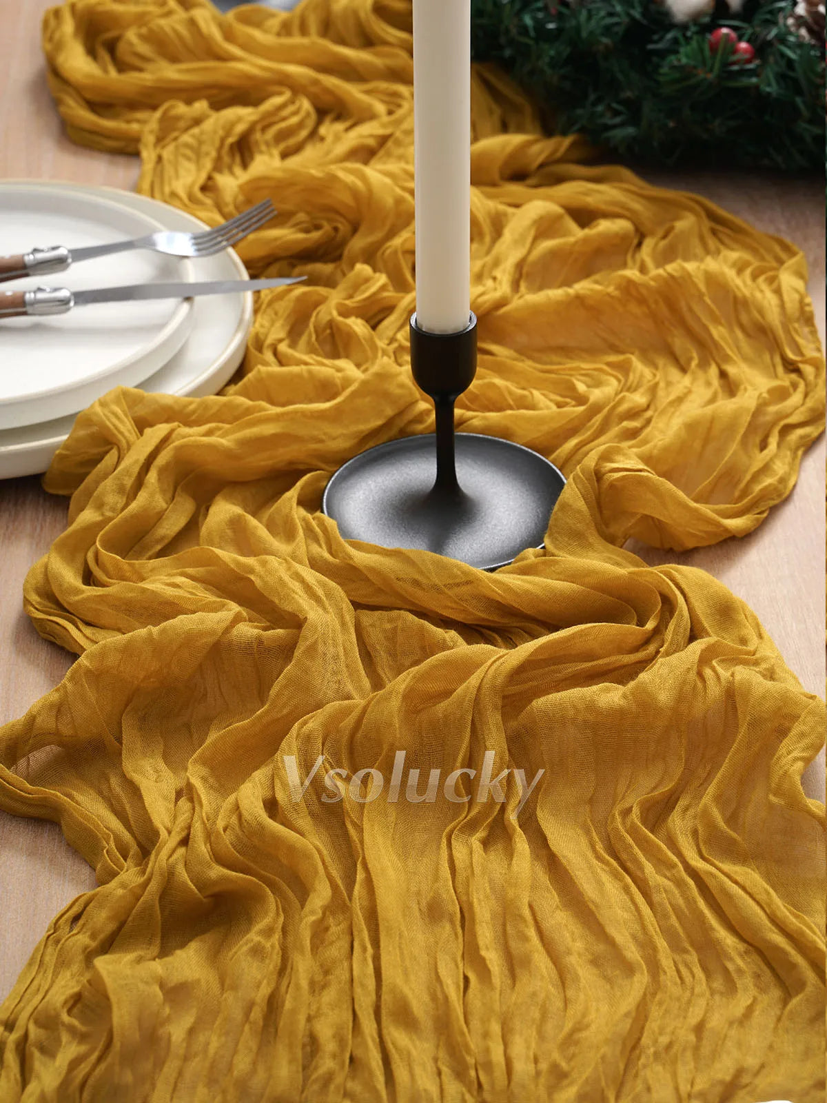 A golden yellow crinkle gauze cheesecloth table runner draped on a wooden surface with silverware and a white candle holder.