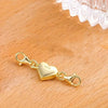 A gold heart-shaped magnetic clasp for necklaces and bracelets resting on a wooden surface.