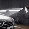 A heavy-duty pressure washer gun sprays water onto a car surface in a dark garage setting.