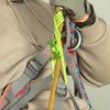 A hand wearing a glove is adjusting a yellow climbing rope attached to a harness and carabiner.
