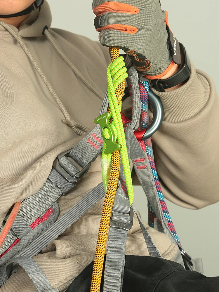 A hand wearing a glove is adjusting a yellow climbing rope attached to a harness and carabiner.