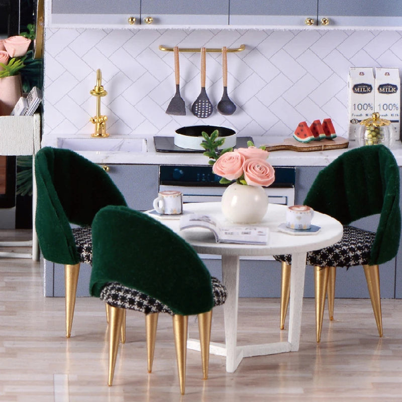A white dining table set with green velvet chairs and a wooden dollhouse miniature building kit.