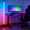 A computer setup featuring an LED RGB corner floor lamp and desk lighting in a dimly lit room.