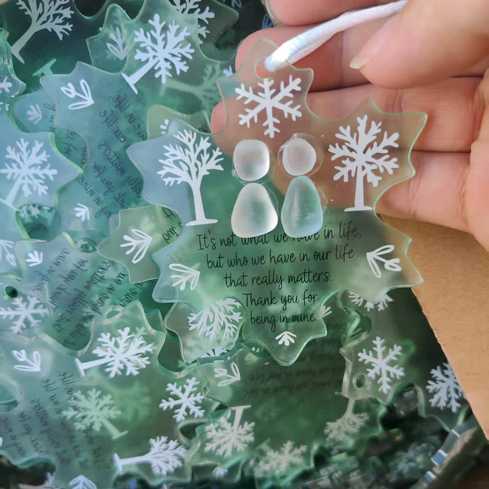 A hand holds a handcrafted snowflake sea glass ornament with engraved text and a tree design.