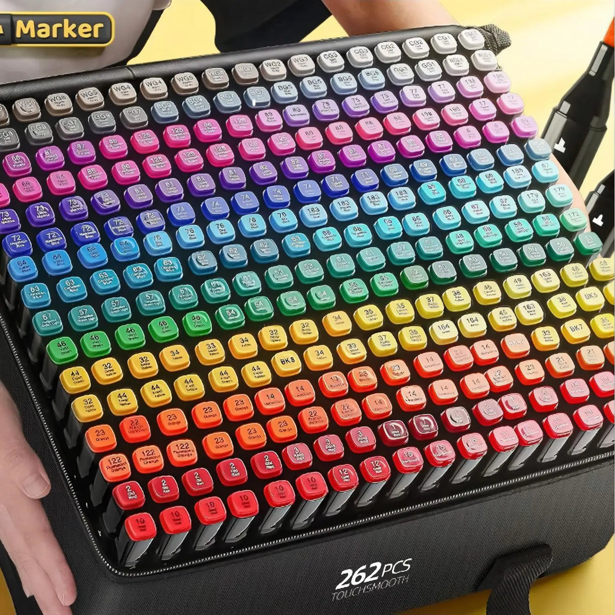 A close-up of a black marker set with 262 paint markers arranged in a rainbow gradient on a yellow background.
