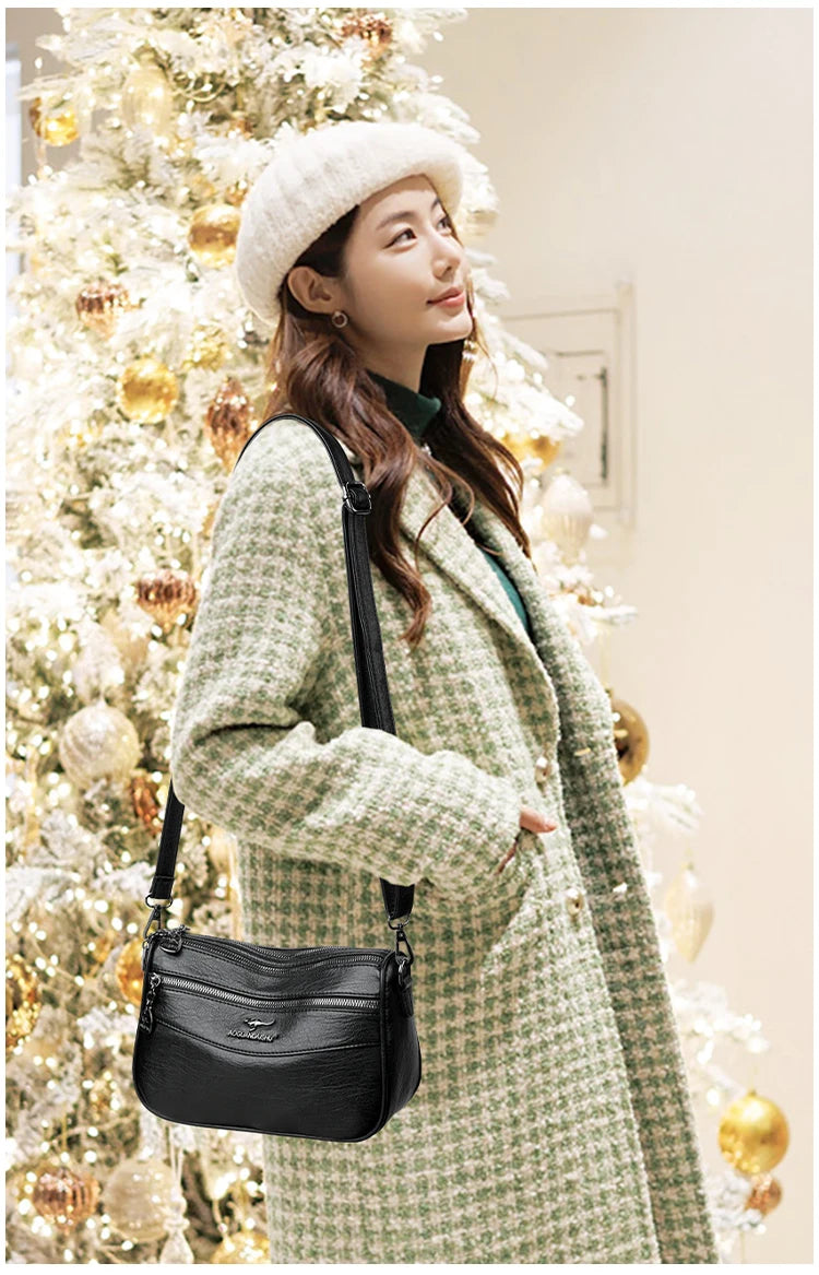 A woman wearing a tweed coat and knit hat holds a black compact square crossbody bag in a festive holiday setting.