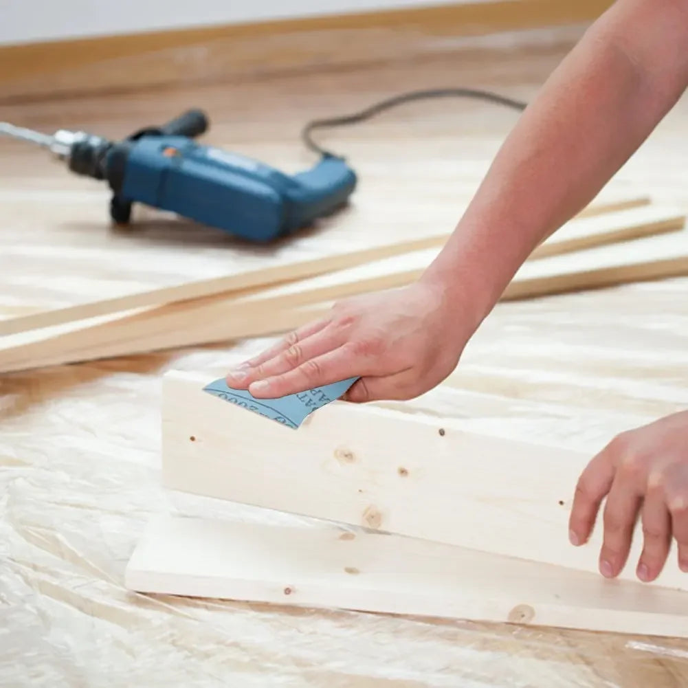 A hand is using a power sander to smooth a piece of wood, demonstrating the use of sandpaper grit.