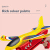 A hand holds a bright yellow and red foam plane launcher toy for kids against a light pink background.