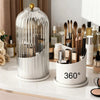 A clear cylindrical makeup brush holder with a dustproof lid and a rotating mechanism sits on a white surface.