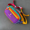 A colorful rainbow striped waterproof nylon fanny pack with a pink zipper and yellow strap lying on a gray surface.