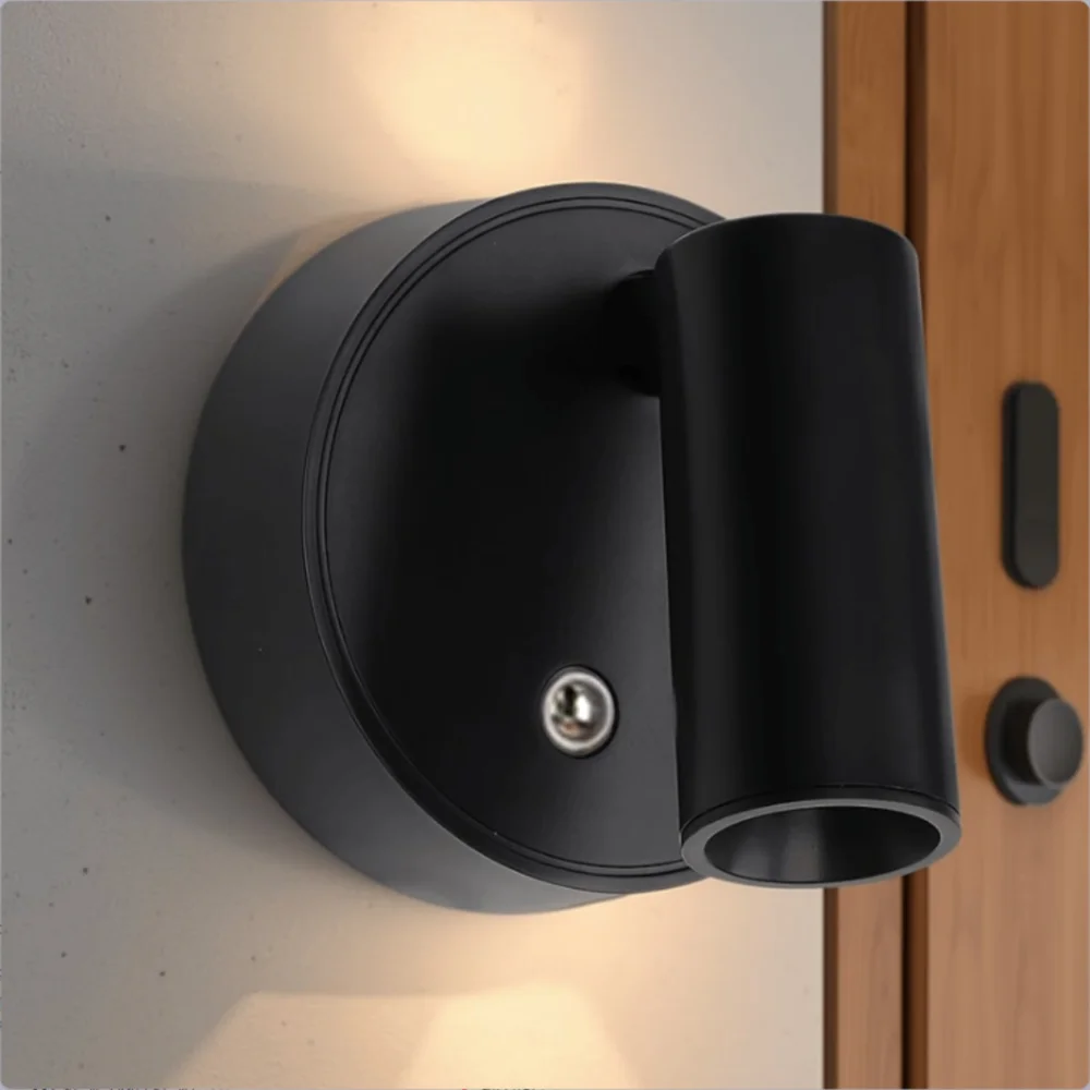 A black rechargeable LED wall lamp with a rotating head is mounted on a light gray wall.