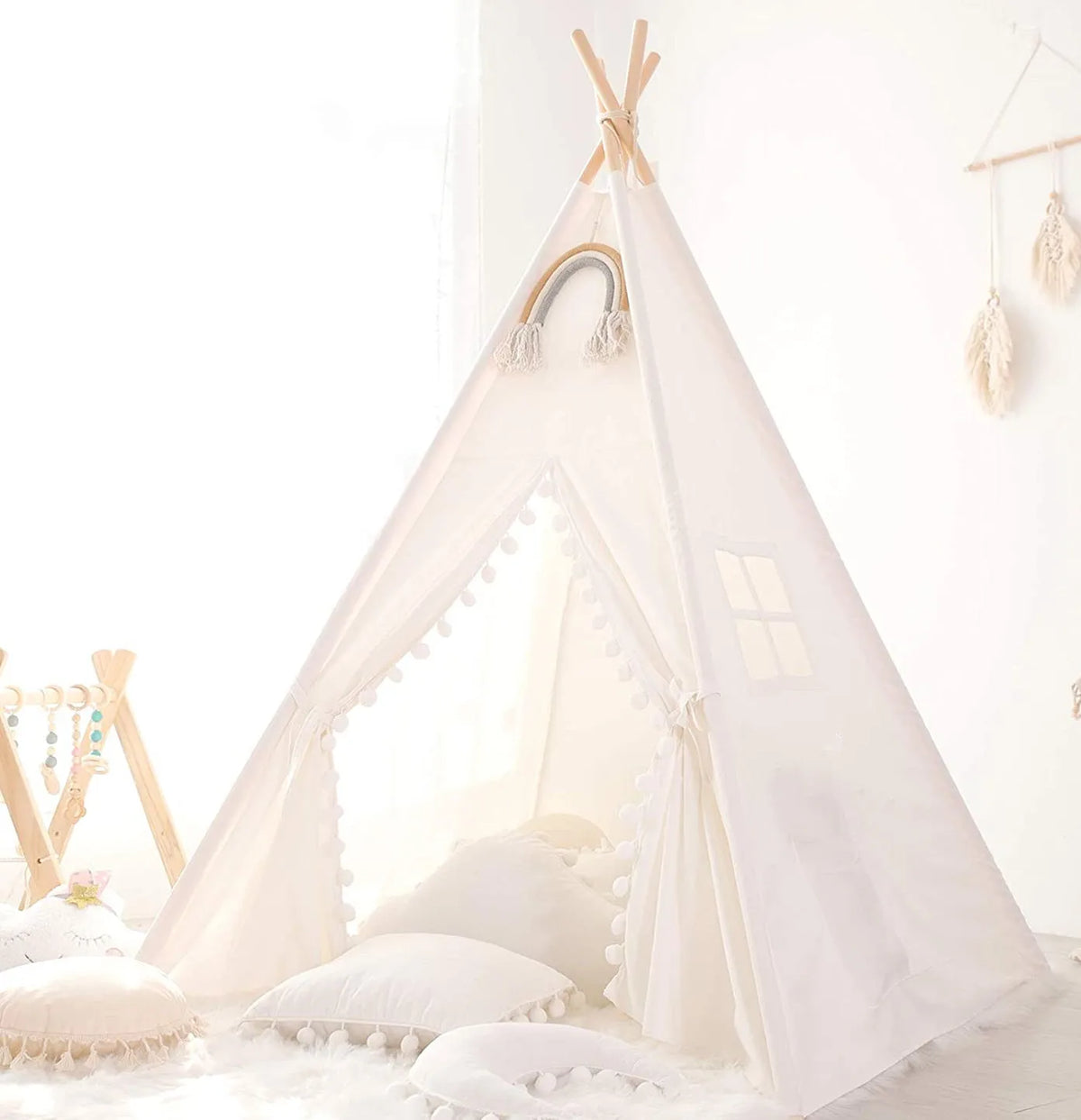 A white kids fold-able play tent with sheer curtains and decorative tassels set up indoors.
