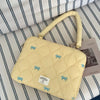 A light yellow quilted laptop shoulder bag with a leather handle and blue bow embellishments resting on striped fabric.
