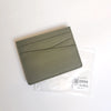A slim, olive green genuine leather card holder wallet is shown inside a clear plastic sleeve.