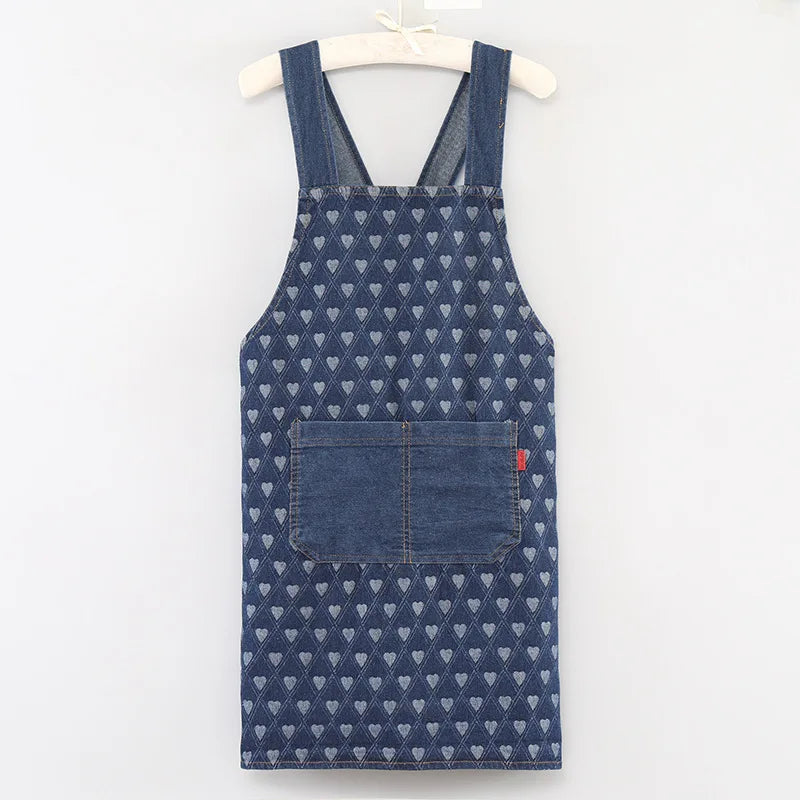 A dark blue denim cross-back apron with a repeating pattern of small white hearts and a chest pocket.